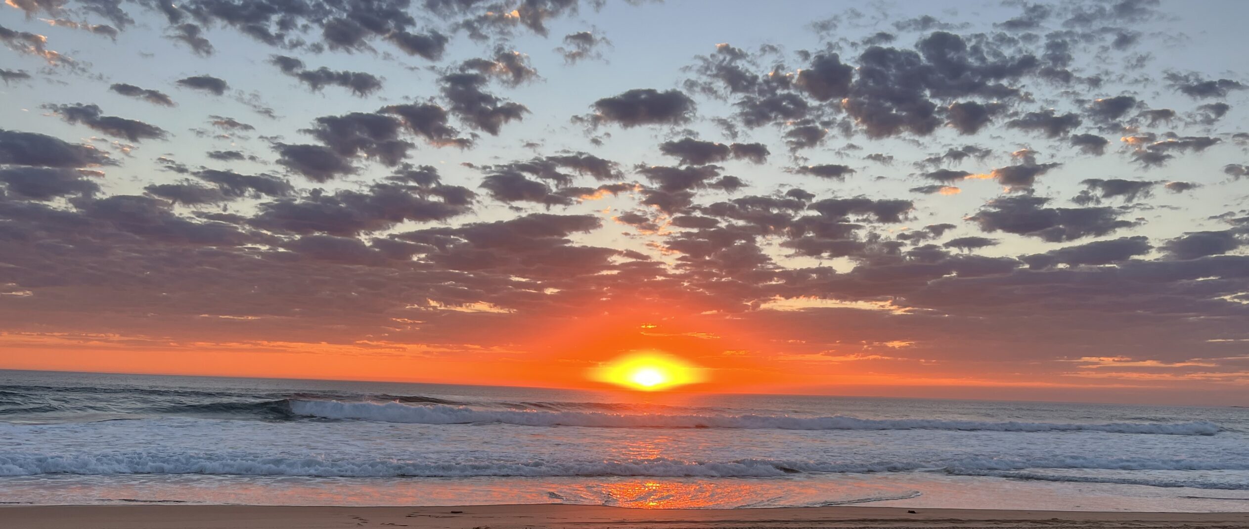 A vibrant orange sun setting over the ocean, with soft waves and scattered clouds in the sky, symbolising guidance.